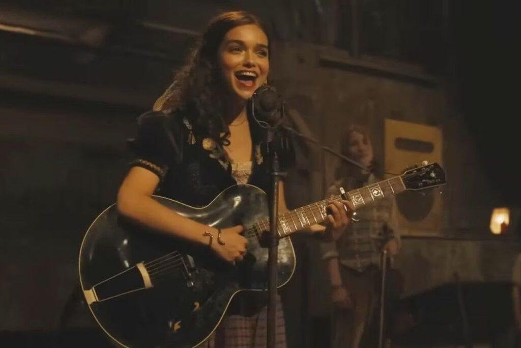 Personagem Lucy Gray cantando feliz ao microfone enquanto toca violão.
