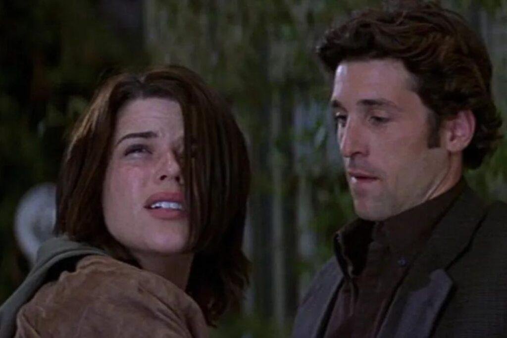 Neve Campbell e Patrick Dempsey em cena Pânico 3, com aulher olhando pra cima com medo e o homem a acalmando.