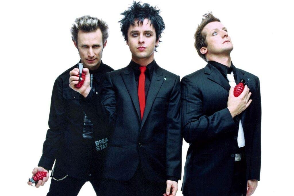 Membros de Green Day com ternos pretos, gravatas vermelhas e granada vermelha nas mãos.
