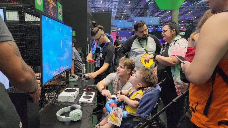 Visitantes em um estande de jogos interativo no Big Festival, com destaque para um jogador com deficiência usando um controle adaptado para videogame, organizado pela AbleGamers Brasil.