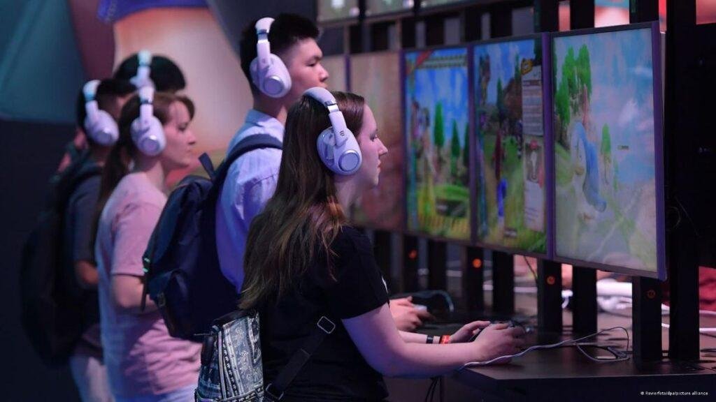 Jogadores concentrados em telas de jogos eletrônicos, utilizando fones de ouvido, em um evento de jogos.