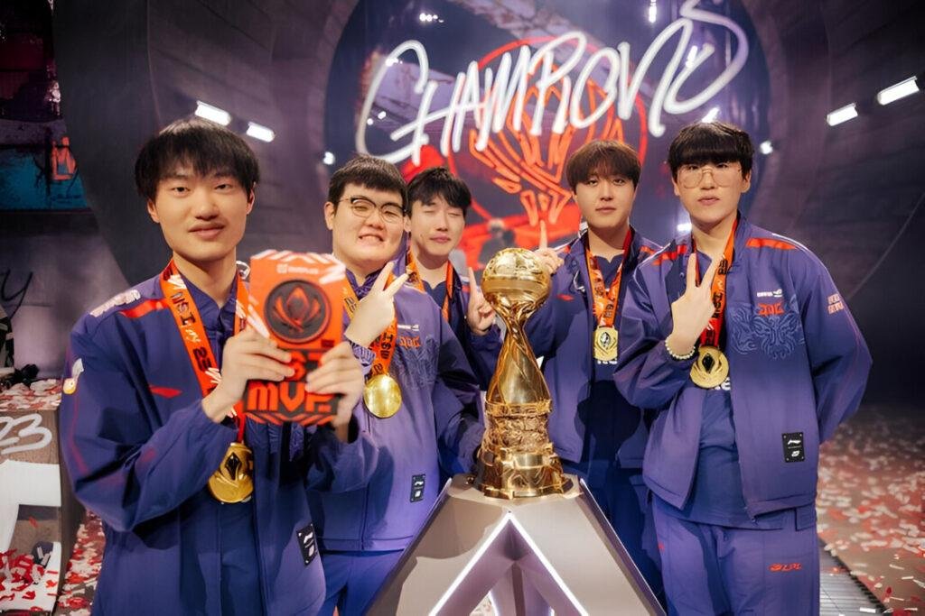 Equipe de eSports celebrando no palco com troféu e prêmio MVP após vencer campeonato, com o termo "CHAMPIONS" ao fundo.