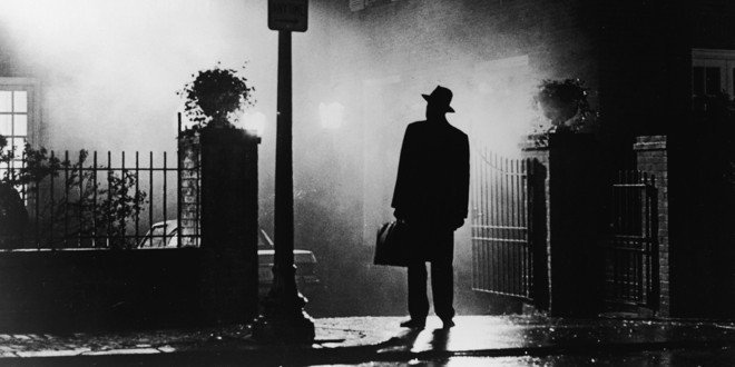 Um homem misterioso de chapéu e sobretudo preto em uma rua escura e enevoada, lembrando a atmosfera sombria do que muitos consideram o melhor filme de terror da história.