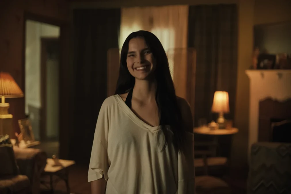 A atriz Inde Navarrette com cabelos longos e escuros sorrindo de forma macabra em uma sala com pouca luz, cena de um filme que concorre ao título de melhor filme de terror.