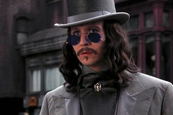 Gary Oldman como Drácula, usando um chapéu alto e óculos escuros redondos e azuis.