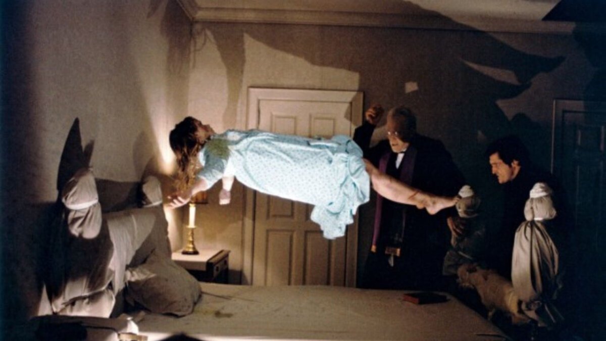 A jovem Regan levitando acima de sua cama, assistida por dois padres chocados mostra como O Exorcista é uma das maiores adaptações de terror.