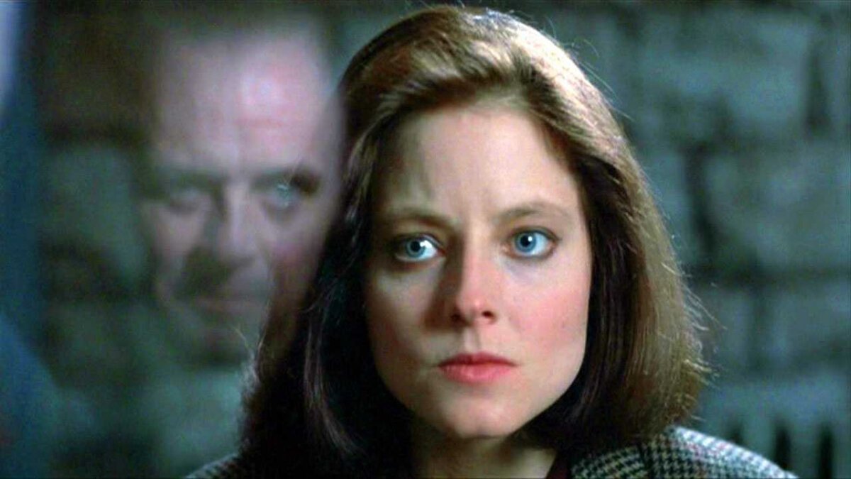 Um close-up de Jodie Foster como Clarice Starling, com o reflexo de Anthony Hopkins como Hannibal Lecter atrás dela.